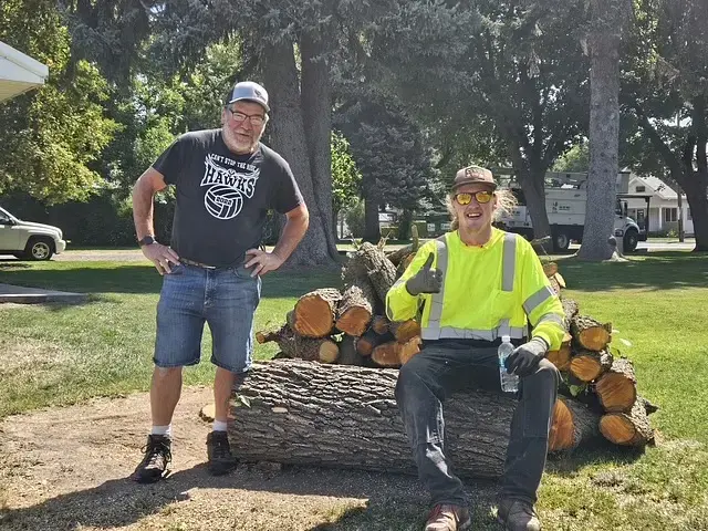 Two J&J's Tree Service crew members with cut logs after a removal